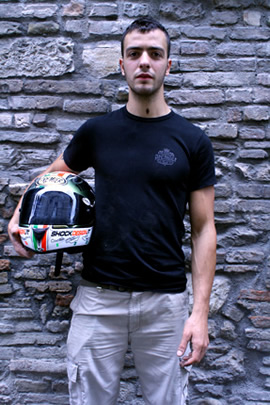 Michele Magnoni holds his helmet in front of cobbled wall.